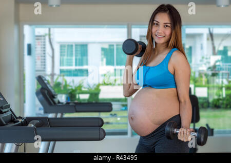 Ritratto di asian femmine gravide di fare esercizio nella sala sportiva, sollevamento pesi, sana maternità concept Foto Stock
