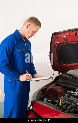 Mechanic in piedi accanto a AUTO sulla scrittura di appunti Foto Stock