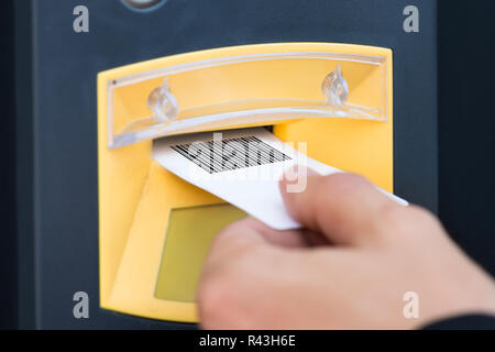 Persona della mano inserire biglietto in slot di parcheggio Foto Stock