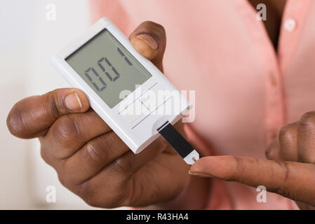 Mano che tiene il dispositivo per misurare lo zucchero nel sangue Foto Stock