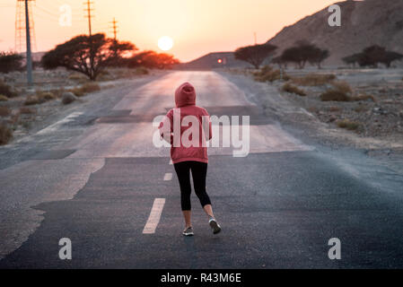 Ragazza che corre in sunset indossare una felpa con cappuccio di colore rosa Foto Stock