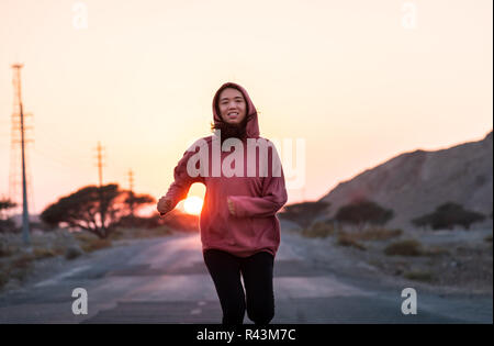 Ragazza che corre in sunset indossare una felpa con cappuccio di colore rosa Foto Stock