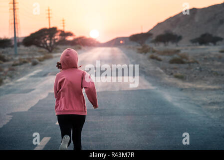 Ragazza che corre in sunset indossare una felpa con cappuccio di colore rosa Foto Stock