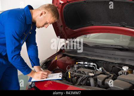 Mechanic in piedi accanto a AUTO sulla scrittura di appunti Foto Stock