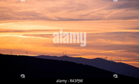Vista laterale delle sagome delle gamme della montagna al tramonto del tempo con generatori di vento su di essi. La Grecia Foto Stock