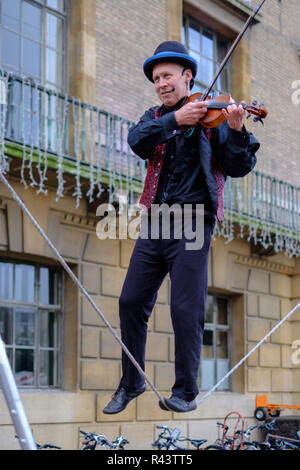 Un cambridge street esecutore suona il violino mentre a piedi una slackline sul mercato Cambridge, Regno Unito. Foto Stock