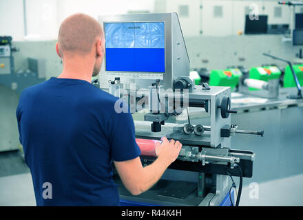 Lavoratore in una stampa e premere Centro utilizza la piastra macchina di montaggio per fissare il polimero piastra di sfiato su un cilindro di stampa. Scena che mostra il montaggio di pri Foto Stock