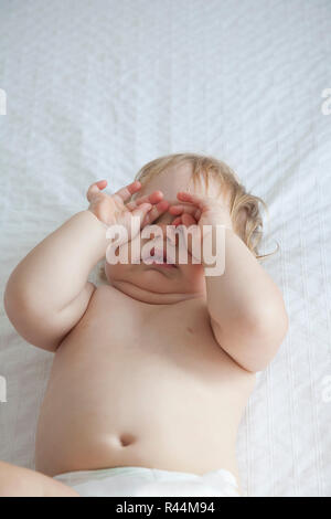 Baby di toccare gli occhi sul letto bianco Foto Stock