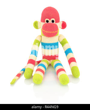 Carino fatti a mano di scimmia a crochet doll isolato su sfondo bianco con ombre di riflessione. Giocoso crochet rosa verde blu bianco monkey seduta su bianco u Foto Stock