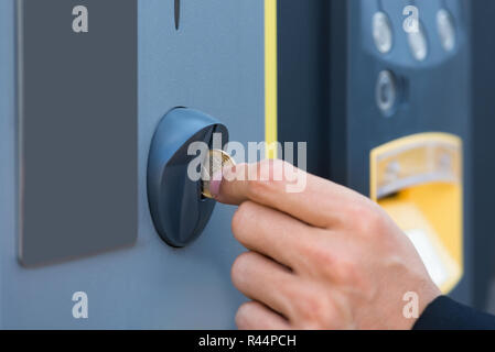 Persona della mano inserire moneta sul parchimetro Foto Stock