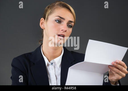 Scioccato giovane imprenditrice lettura la Lettera alla scrivania Foto Stock