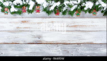 Coperta di neve bordo superiore del Natale rami sempreverdi e il cookie di decorazioni su bianco legno vintage Foto Stock