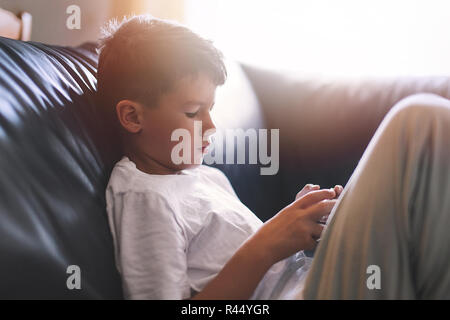 Piccolo ragazzo solitario gioca su smartphone sul divano di casa Foto Stock