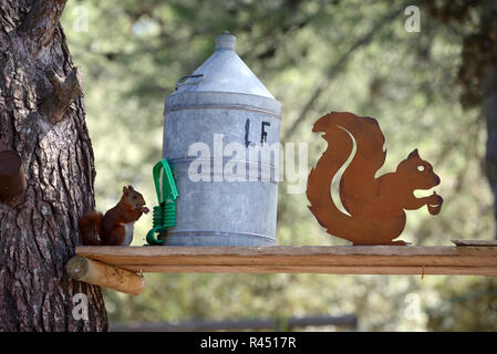 Eurasian scoiattolo rosso Sciurus vulgaris, alimentando ad alimentatore fatti in casa e metallo scultura scoiattolo Foto Stock