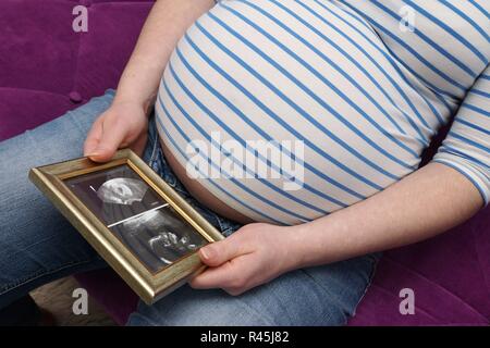 La donna incinta è seduto con l'immagine ad ultrasuoni del suo bambino su un divano Foto Stock