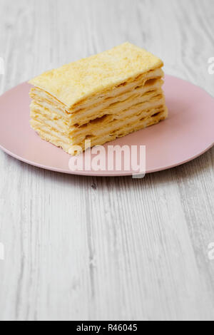 Pezzo di torta di Napoleone sulla piastra rosa bianca su sfondo di legno, close-up. Foto Stock