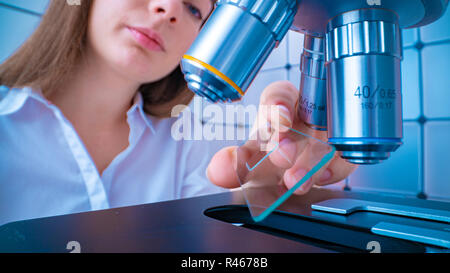 Scienziato analizzando vetrino del microscopio in laboratorio. Giovane donna tecnico sta esaminando un campione istologico, una biopsia in laboratorio di cancro ri Foto Stock