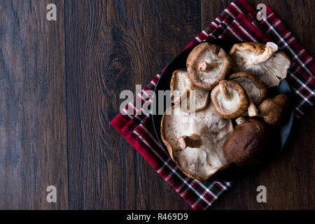 Funghi shiitake nella piastra di colore nero scuro sulla superficie di legno. Alimenti biologici. Foto Stock