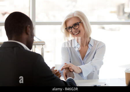 Sorridente maturo imprenditrice caucasica tenendo la mano di afro-un Foto Stock