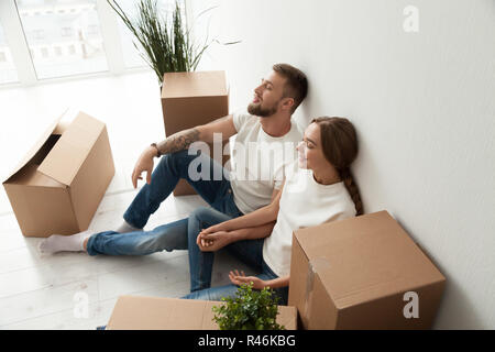 Stanco giovane seduto appoggiato contro la parete in un nuovo appartamento Foto Stock