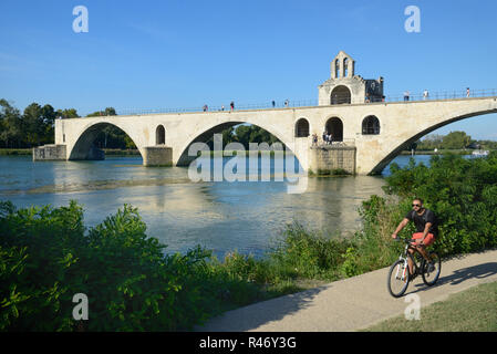 Ciclista Escursioni in bicicletta lungo il fiume Rodano passato il Pont d'Avignon o punto Saint-Bénézet pietra medievale ponte sul Rodano ad Avignone Provenza Foto Stock