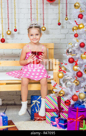 Ragazza seduta su una panchina con un regalo in mano un nevoso di alberi di Natale Foto Stock