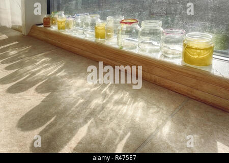 Le banche con acqua colorata per il lavaggio delle spazzole in corrispondenza di una finestra con un sole luminoso Foto Stock