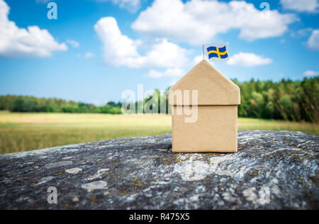 Casa di cartone con la bandiera svedese su una roccia di muschio. Estate scandinava paesaggio. Foto Stock