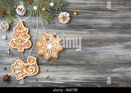 Gingerbread cookies e le decorazioni di Natale sono appesi su abete su sfondo di legno, copia dello spazio. Messaggio di saluto festivo card. Foto Stock