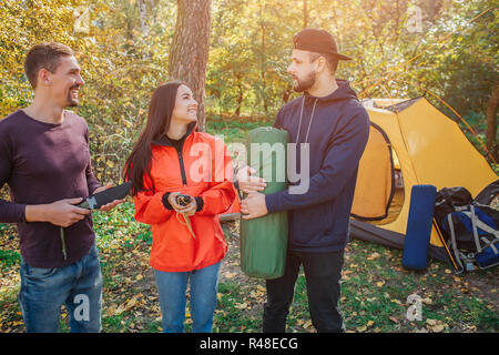 Foto di tre amici nella foresta. Giovane donna sorride e guarda al ragazzo barbuto. Egli detiene il sacco a pelo. Un altro giovane uomo detiene il coltello. Foto Stock