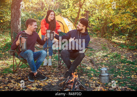 Tre amici sono insieme nella foresta. Essi detengono coppe insieme e guardare a ogni altro. Alcuni di loro tenere thermoses in mani. Sono felice. Foto Stock