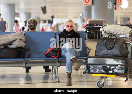 Viaggiatori femmina tramite telefono cellulare mentre si è in attesa in aeroporto. Foto Stock