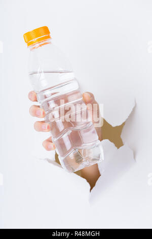 Donna mano con bottiglia di acqua attraverso un foro nella carta Foto Stock