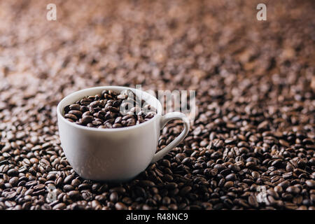 Una tazza riempita con i chicchi di caffè su uno sfondo completamente costituito da chicchi di caffè Foto Stock