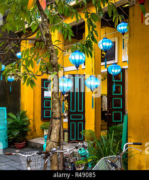 Parte anteriore di Hoi An edificio giallo con aqua blue lanterne e biciclette parcheggiate nella parte anteriore. Foto Stock