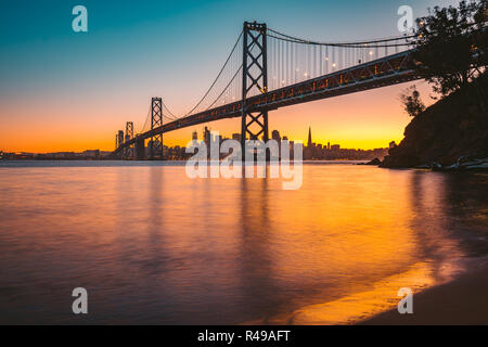 Classic vista panoramica dello skyline di San Francisco con il famoso Oakland Bay Bridge illuminato nel bellissimo golden luce della sera al tramonto in estate Foto Stock