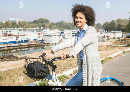 Ritratto di felice e splendida razza mista nero donna guidare la bicicletta sulla riva del fiume. Foto Stock