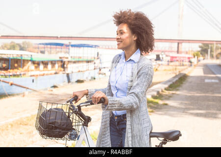 Razza mista nero donna con bicicletta godendo del tempo libero vicino al fiume. Foto Stock