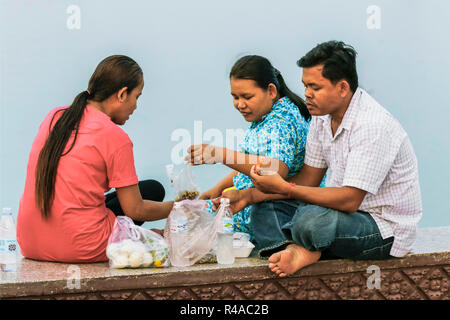 Due donne e uomo avente sunset drinks e spuntini sul Mekong Riverfront Promenade; Preah Sisowath Quay, centro della città di Phnom Penh, Cambogia Foto Stock