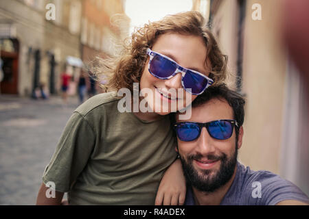 Ragazzo sorridente e suo padre tenendo selfies al di fuori Foto Stock