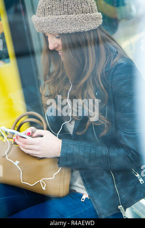 Giovane donna con il suo telefono cellulare mentre si è in attesa per la città in autobus Foto Stock