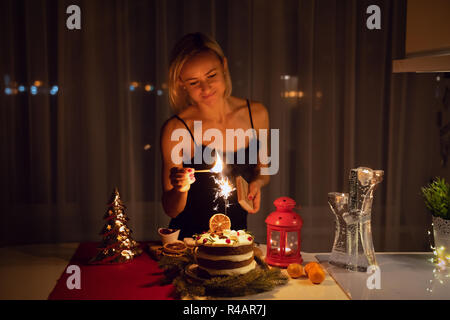 Giovane donna una illuminazione Sparkler nella torta di notte al tempo di Natale Foto Stock