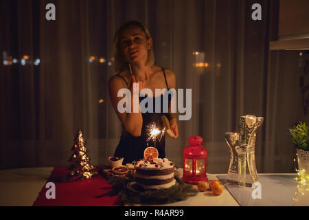 Giovane donna una illuminazione Sparkler nella torta di notte al tempo di Natale Foto Stock