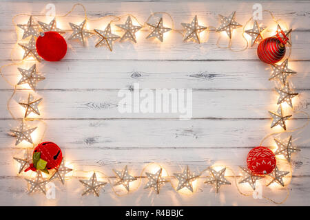 Una stringa di golden star le luci di Natale e baubles rosso, su un destressed woodern sfondo, creando un bordo attorno ad uno spazio vuoto per la copia Foto Stock