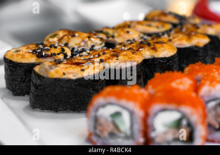 Cotti i sushi giapponesi i rotoli cosparso con semi di sesamo close-up con sfondo sfocato Foto Stock