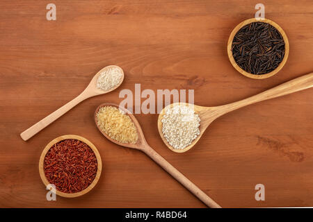 Rosso a grani lunghi Camargue Riso paella bianco bomba, riso parboiled, risotto carnaroli, e selvaggio riso nero, girato da sopra al buio su un sfondo di legno Foto Stock