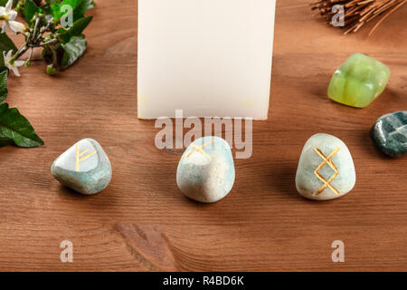 Un primo piano di Norse rune, pietre con simboli utilizzati in Wicca e altri magic e per la divinazione, con una candela e cristalli al buio su un sfondo rustico Foto Stock