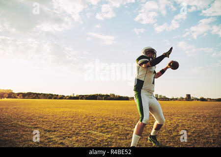 American Football quarterback facendo una lunga gittata durante la pratica del team su un campo sportivo nel pomeriggio Foto Stock
