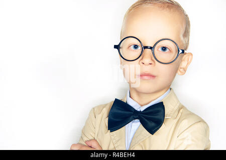 Grazioso piccolo ragazzo biondo vestito come un professore che indossa un abito, bowtie e bicchieri in piedi con sicurezza contro uno sfondo bianco Foto Stock