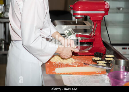 Close-up sulle mani del pasticcere decorare la torta con ribes rosso e una foglia di menta prima di servire. Foto Stock